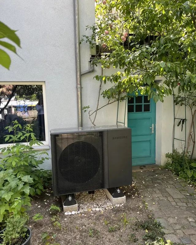 Dunkle Außeneinheit in einem begrünten Innenhof neben einer grünen Tür