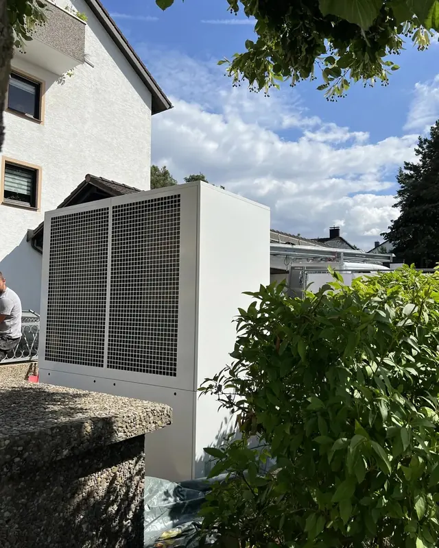 Große Außeneinheit an der Fassade, umgeben von Hecken
