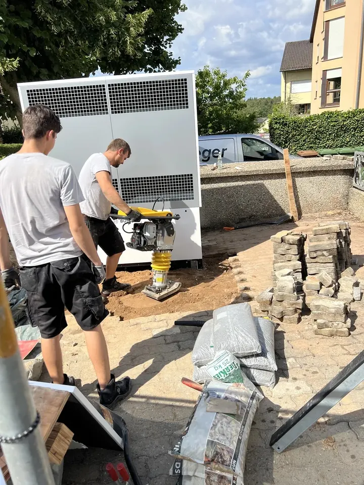 Zwei LEGER-Monteure verdichten den Untergrund für die Außeneinheit einer großen Wärmepumpe