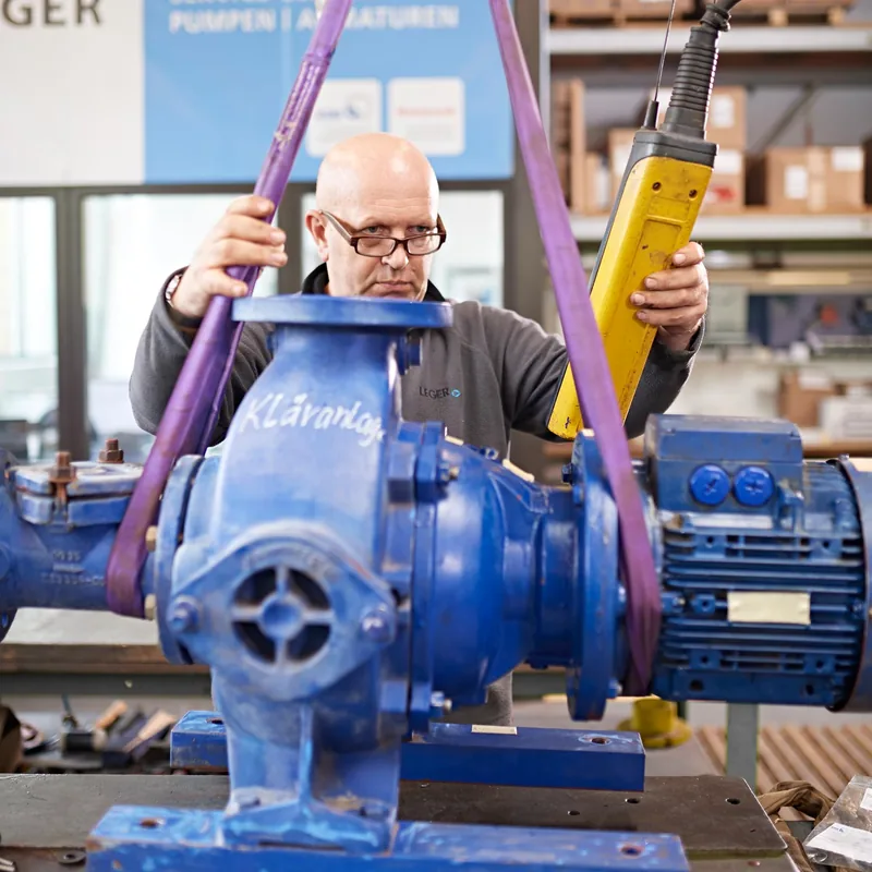 LEGER-Monteur arbeitet mit Hebezeug an einem blauen Pumpenaggregat in der Werkstatt